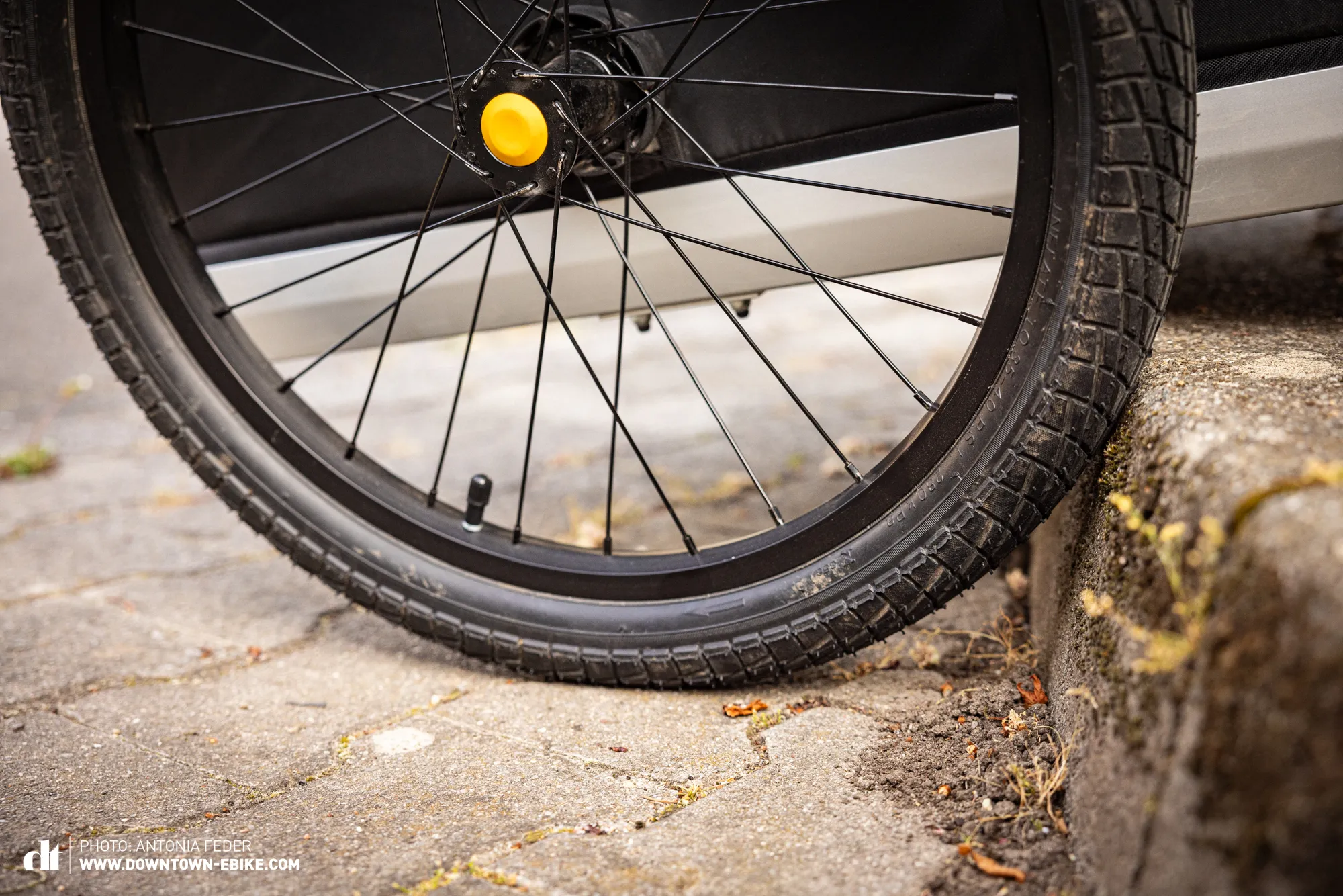 A bicycle trailer tire impacts a curb, a common obstacle in daily use that must be handled smoothly.