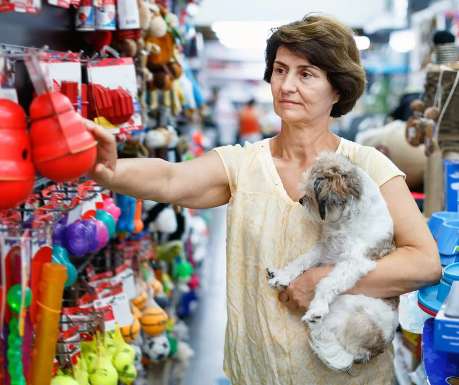 A caring woman gently holds her dog, a golden retriever, as they both look at a selection of dog chew toys, carefully choosing the safest and most appropriate options for playtime.