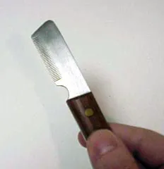A close-up of a grooming tool, likely a stripping knife, held by a hand.