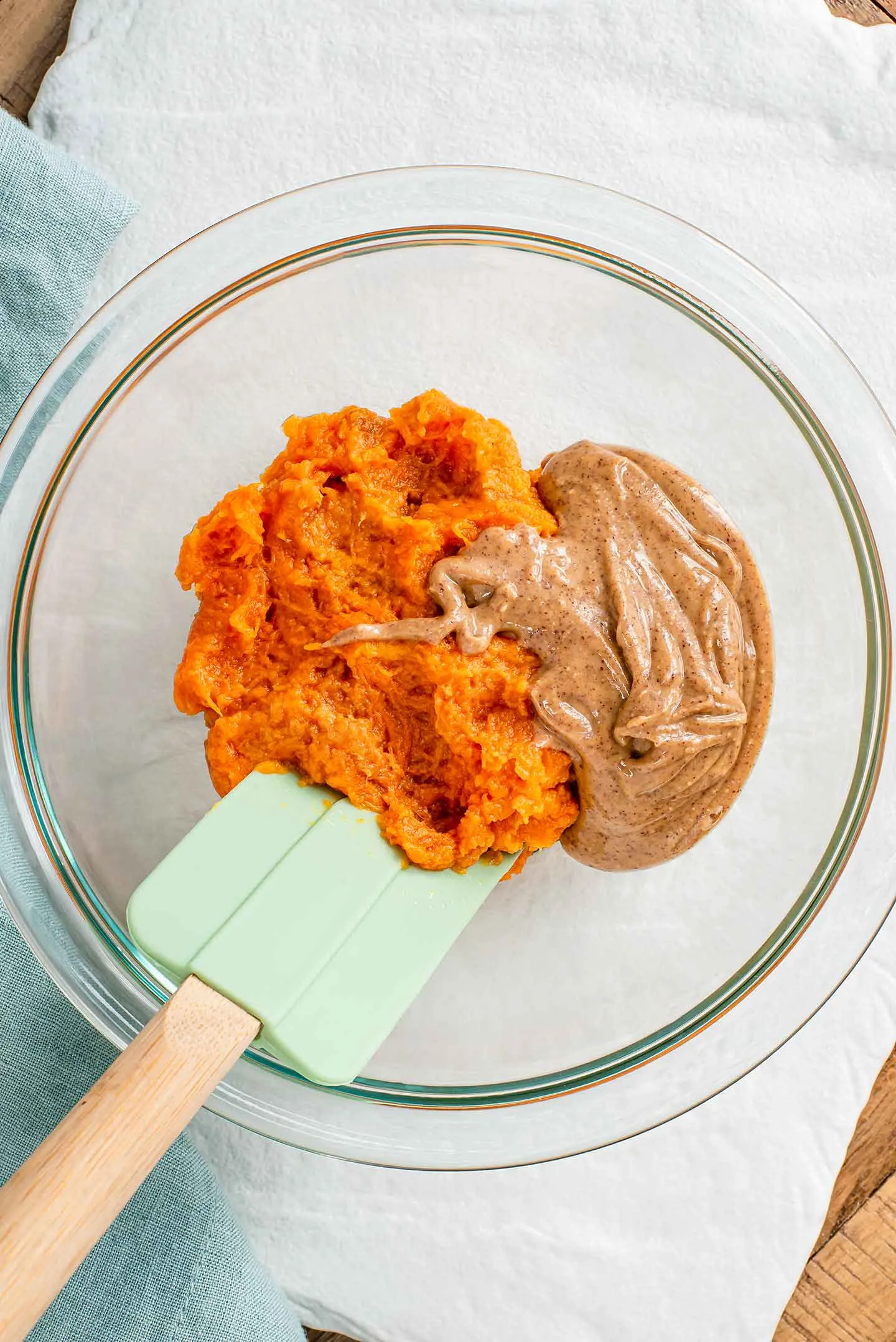 A glass bowl containing mashed sweet potato and smooth peanut butter, ready to be mixed with a silicone spatula for dog treats.