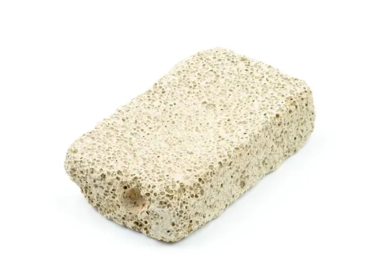 A grey pumice stone being gently rubbed on a fabric surface to collect embedded dog hair