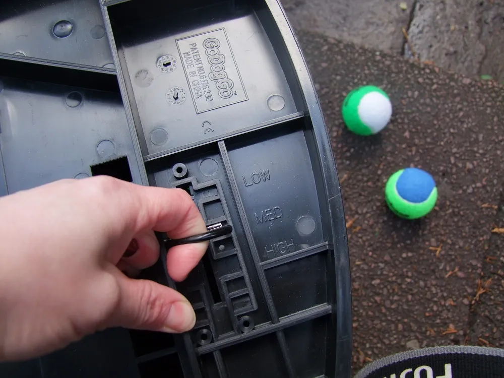 A hand adjusting the launch distance lever on the underside of a GoDogGo automatic dog ball thrower
