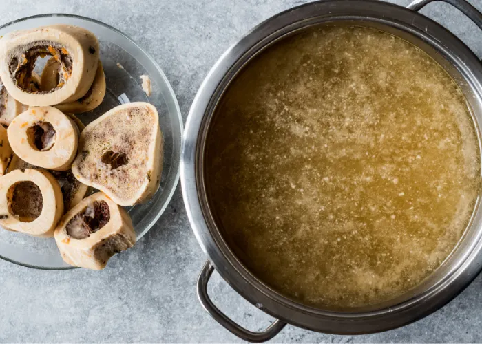 A large pot of homemade bone broth simmering on a stovetop with bones and vegetables