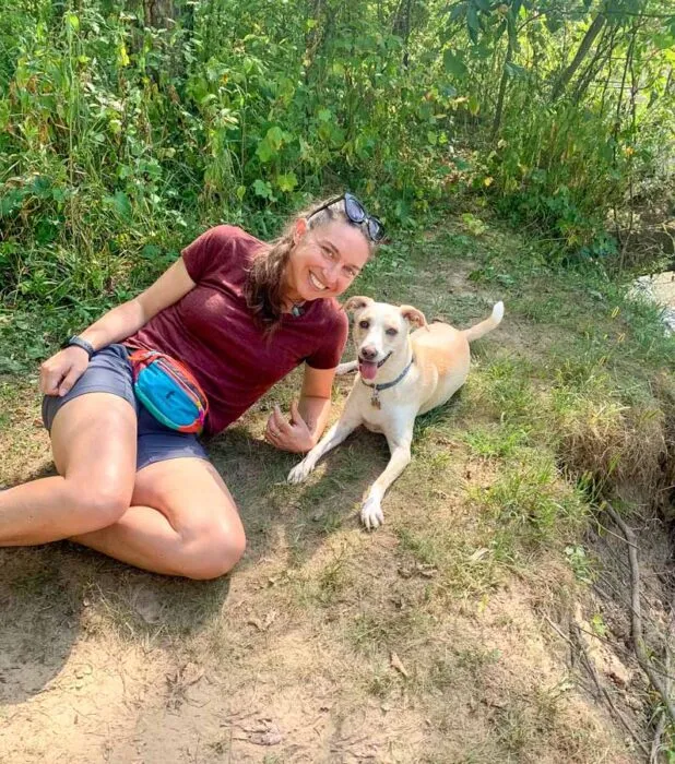 A person and their dog taking a break during a hike, with the person wearing a backpack.