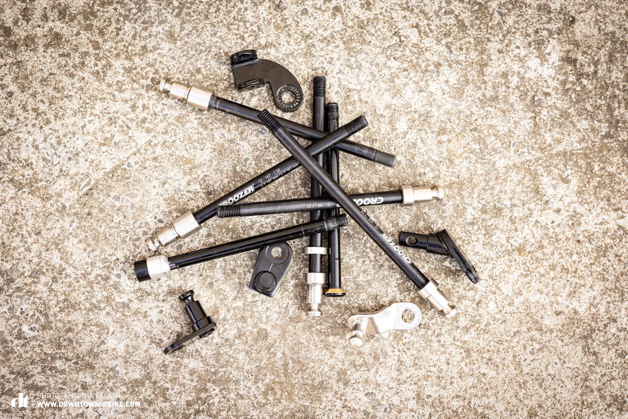 A wide array of thru-axles and hitches for various dog bike trailers and bicycles are displayed.