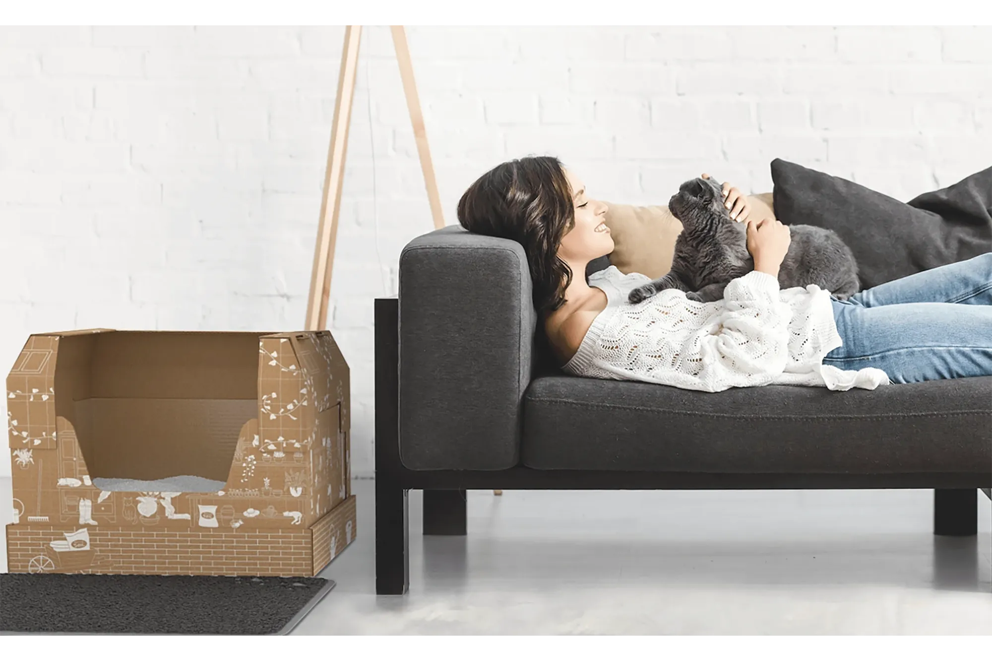 A woman on the couch with her cat and a cardboard litter box on the floor