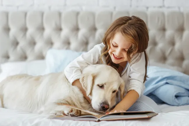 A young girl reading a book with a golden retriever dog by her side, illustrating the joy of dog books for 3rd graders.