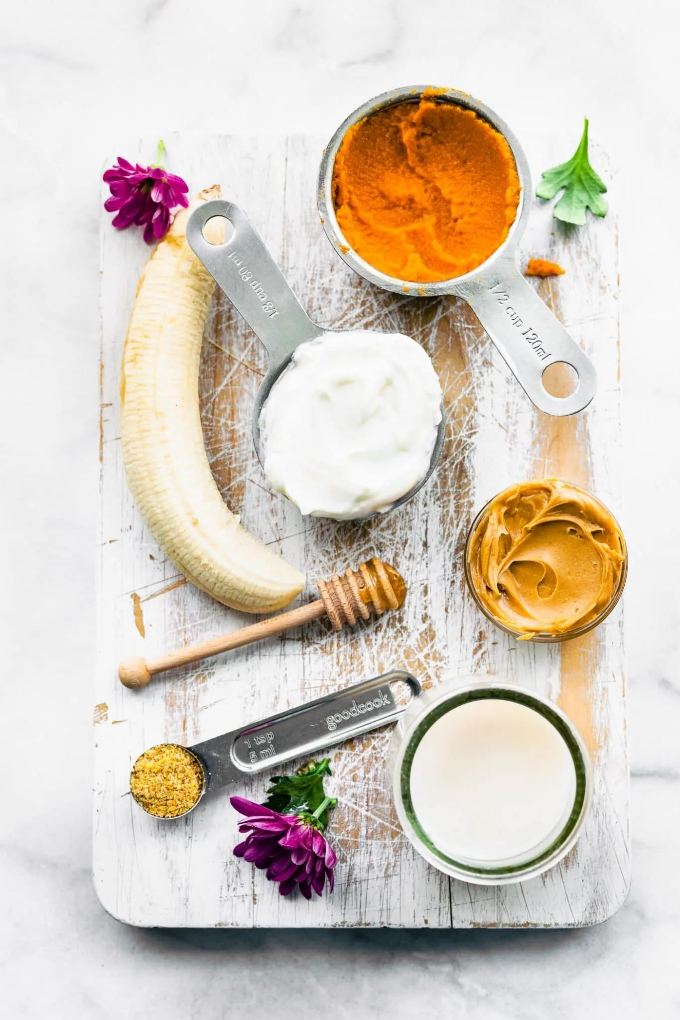 Carefully measured vet-approved ingredients for homemade frozen dog treats, including pumpkin, yogurt, and peanut butter, laid out on a table for preparation.