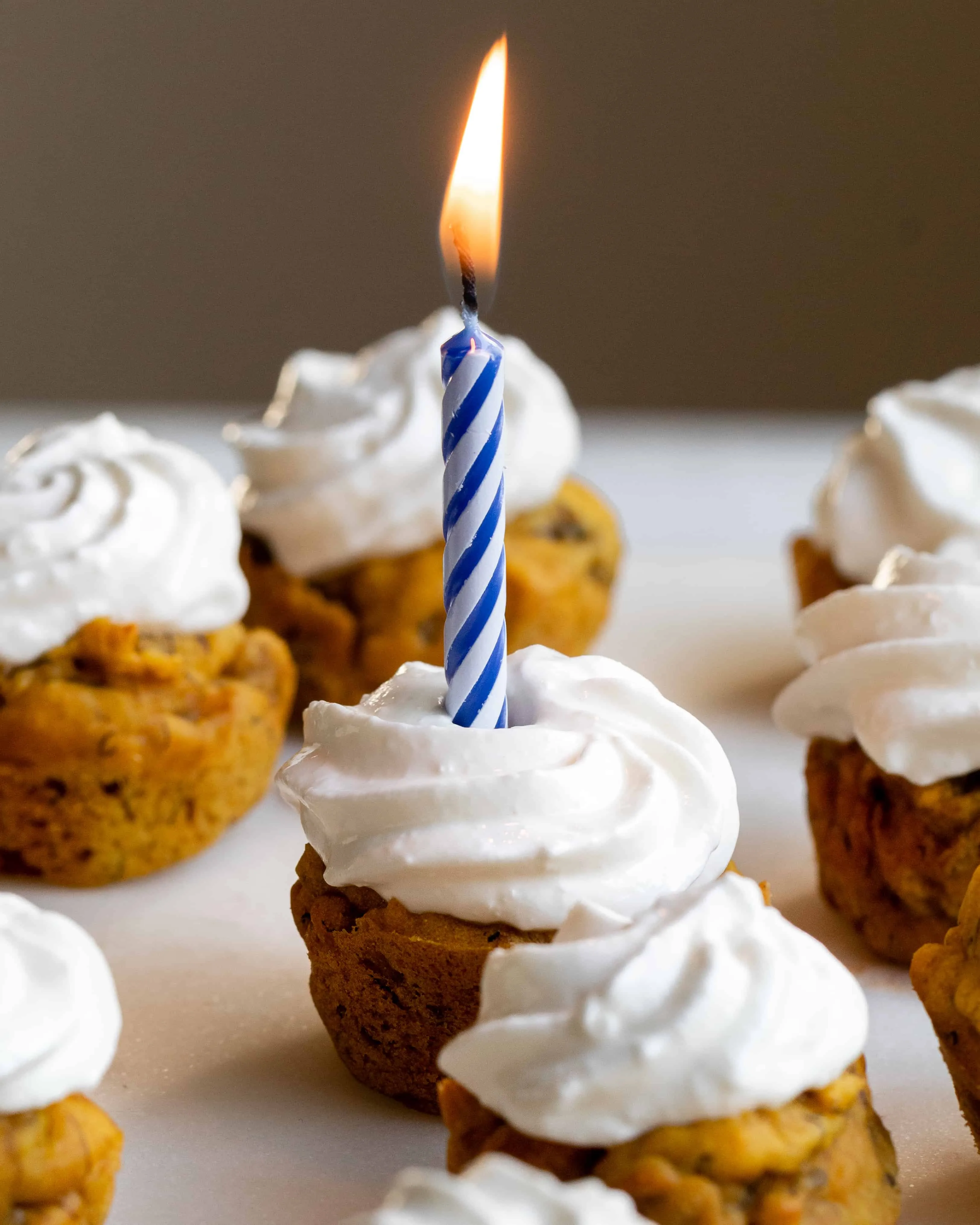 Close up image of a frosted Pumpkin Banana Pupcake on a marble cake stand with a lit birthday candle.