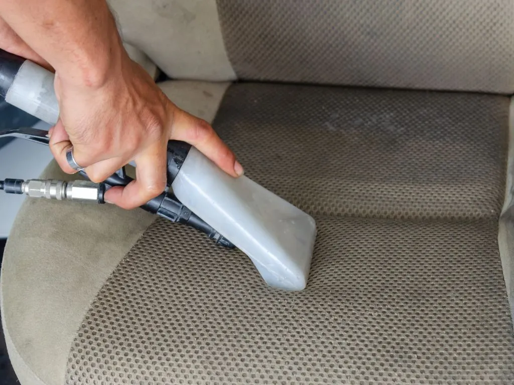 Dog owner vacuuming pet hair from car seat