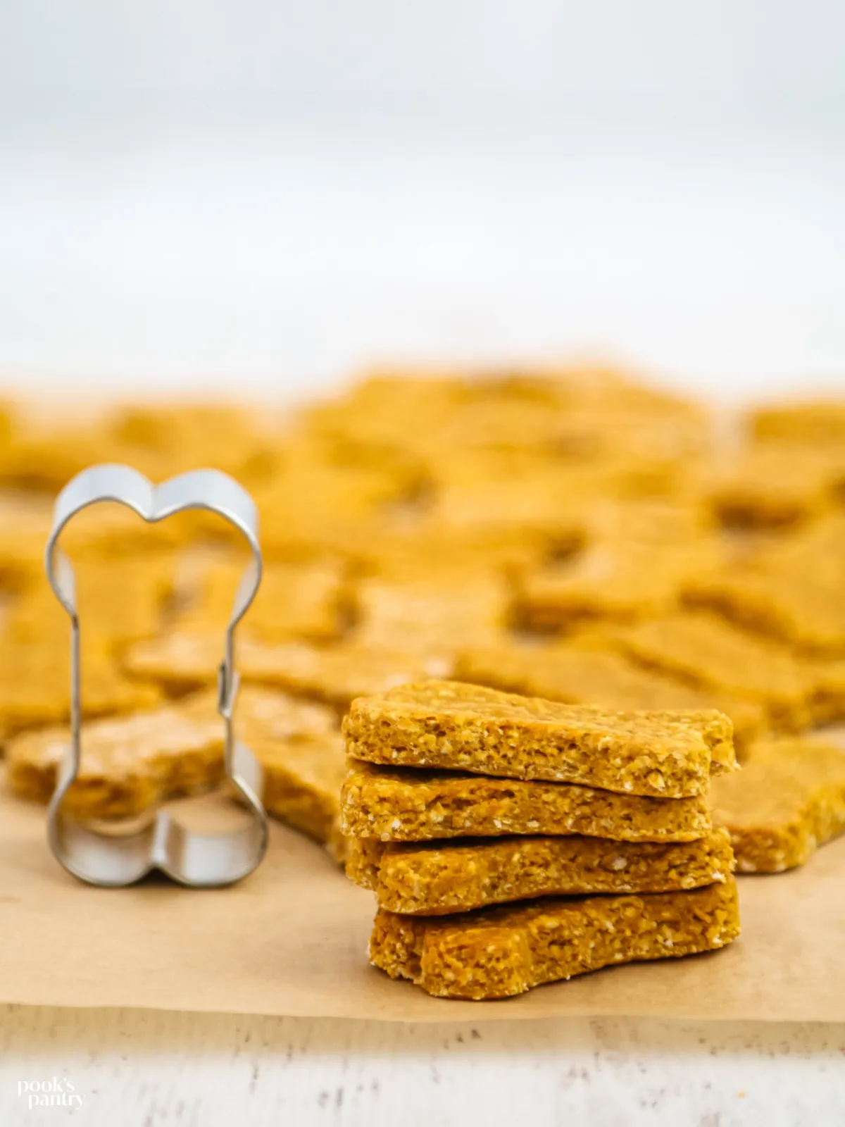 Freshly baked oatmeal pumpkin dog treats stacked beside a bone-shaped cookie cutter, emphasizing simple ingredients