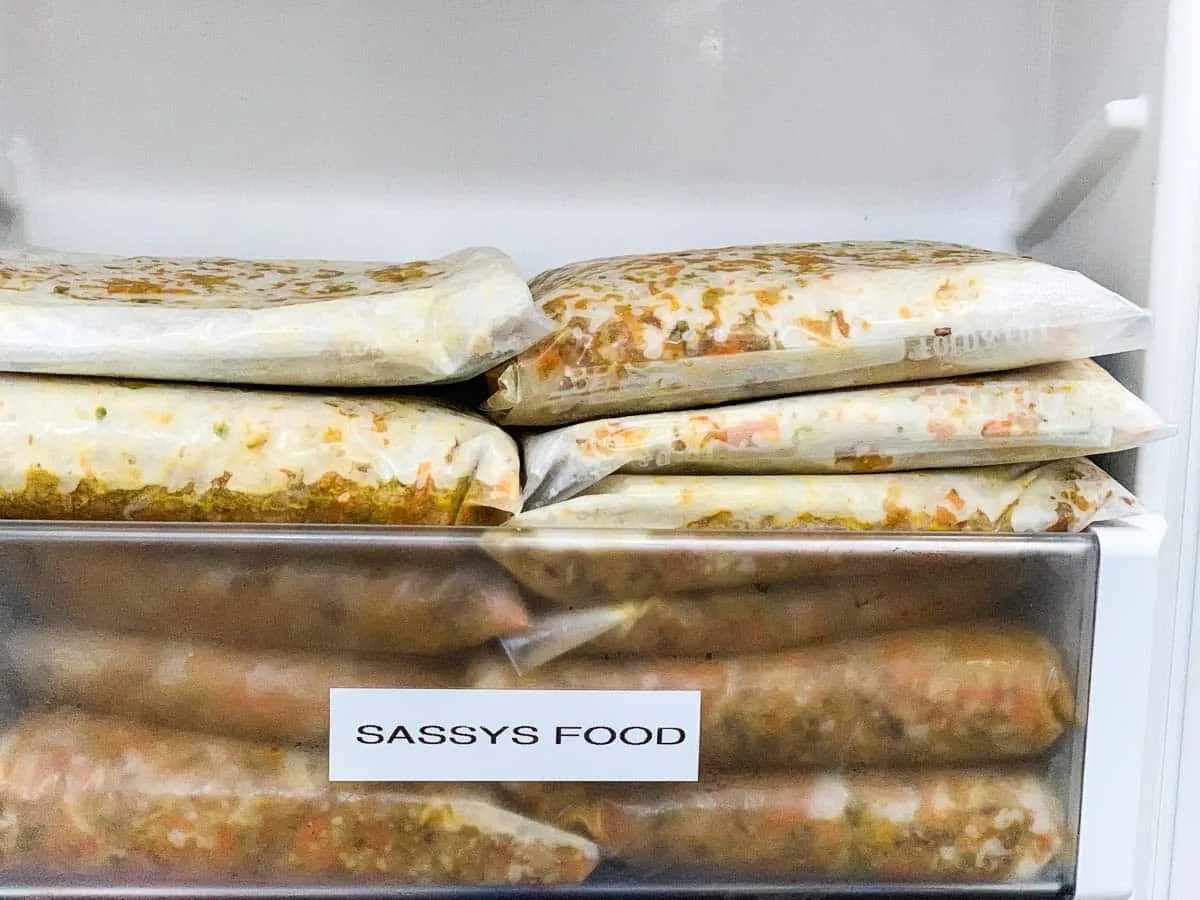 Frozen bags of homemade dog food are stacked inside of a freezer.