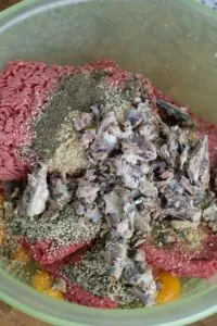 Mixing ground beef, eggs, sardines, and other ingredients in a bowl