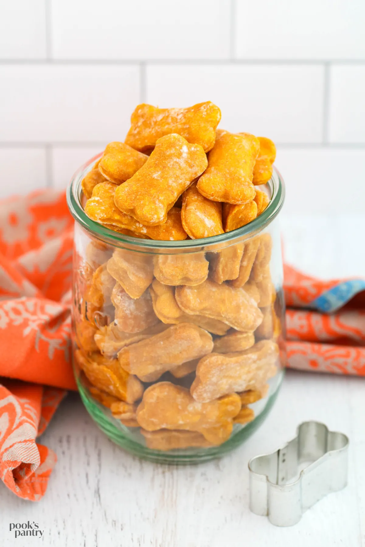 Soft pumpkin dog treats neatly stacked in front of a glass Weck jar, with more treats inside the jar.