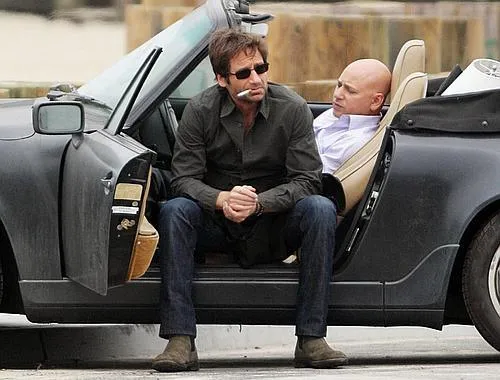 A black and white photograph of Charles Bukowski standing with a woman in a casual setting