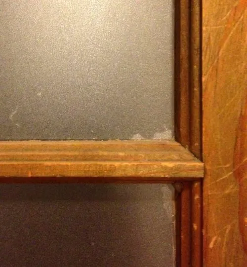 A close-up view of a window pane with "Clear Sand Blast" film installed, showing minor installation flaws.