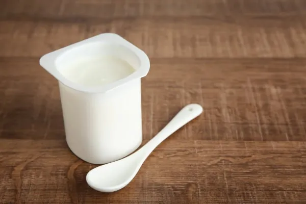 A cup of plain yogurt with a spoon, ready to be used as a pill hider for a dog