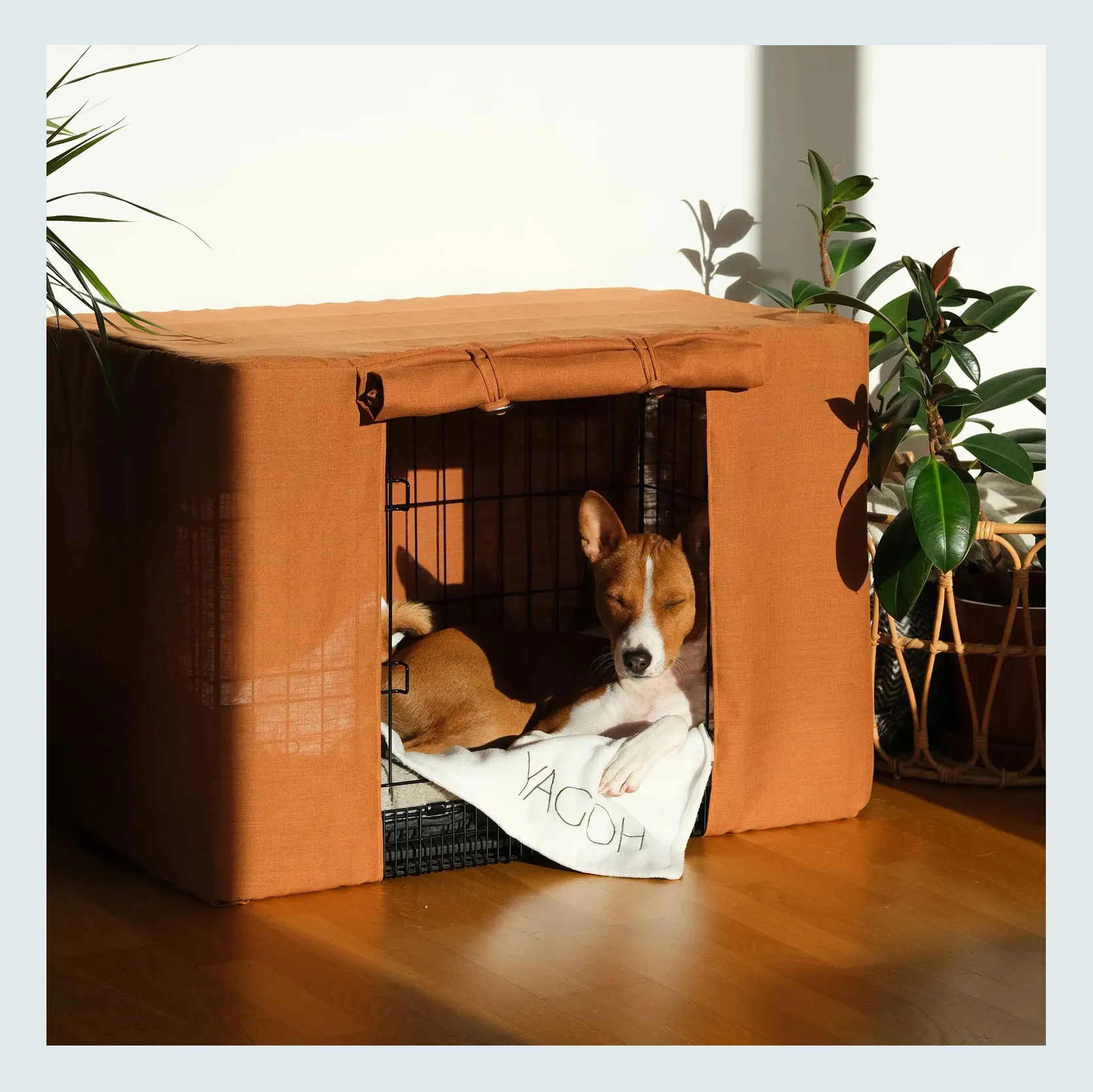 A decorative crate cover draped over a modern white dog crate, blending into a light-filled room.