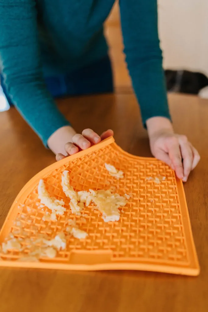 A dog happily licking a banana-filled Lickimat Buddy