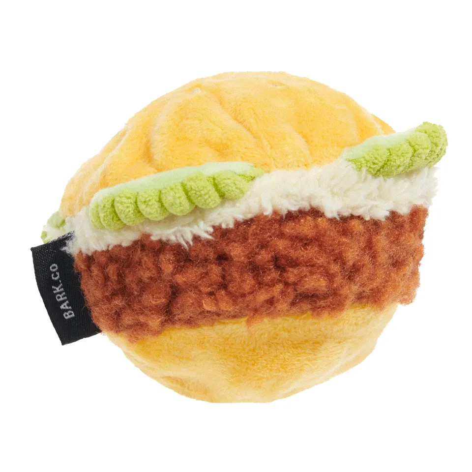 A dog toy shaped like a piece of fried hot chicken, with fabric pickles and a hidden squeaker, designed for strong chewers.