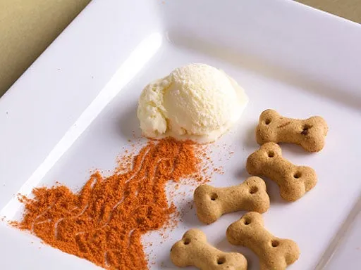 A dog wearing a party hat enjoys a small portion of dog-friendly ice cream on a hot day, celebrating a special occasion.