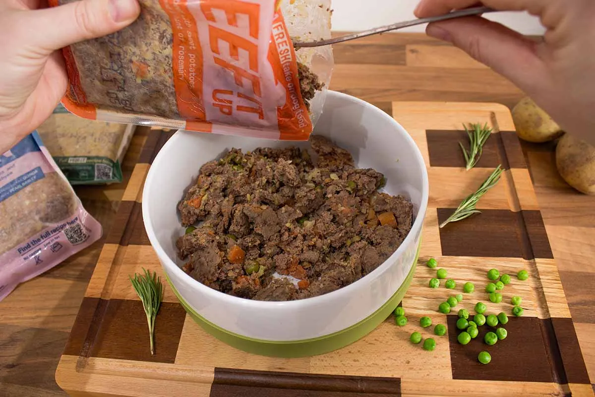 A dog's bowl filled with fresh, prepared dog food, showing visible ingredients like carrots and peas