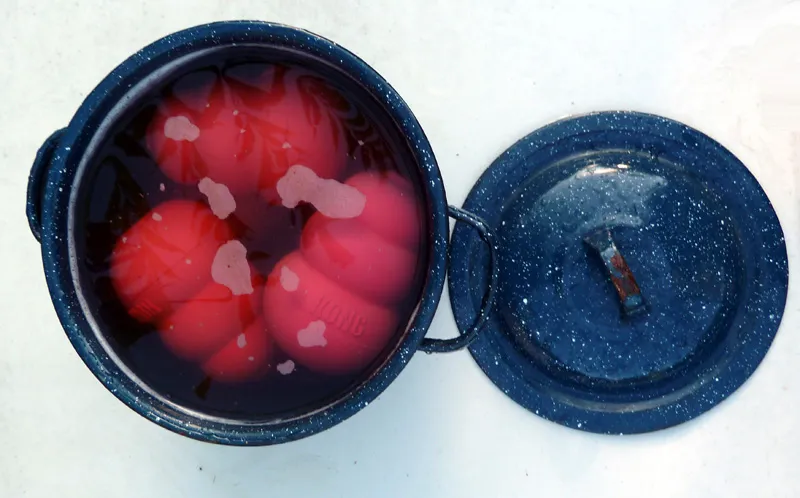 A large pot filled with several red and black Kong dog toys, soaking in a liquid