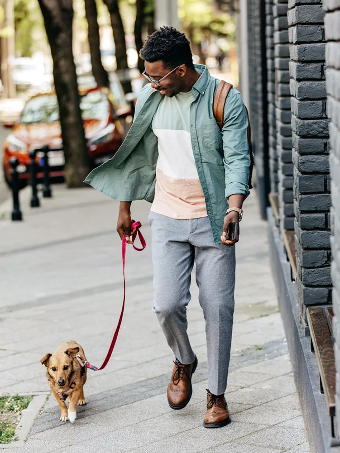 A man walking his dog on a pavement in a city, illustrating urban living challenges for dog owners.