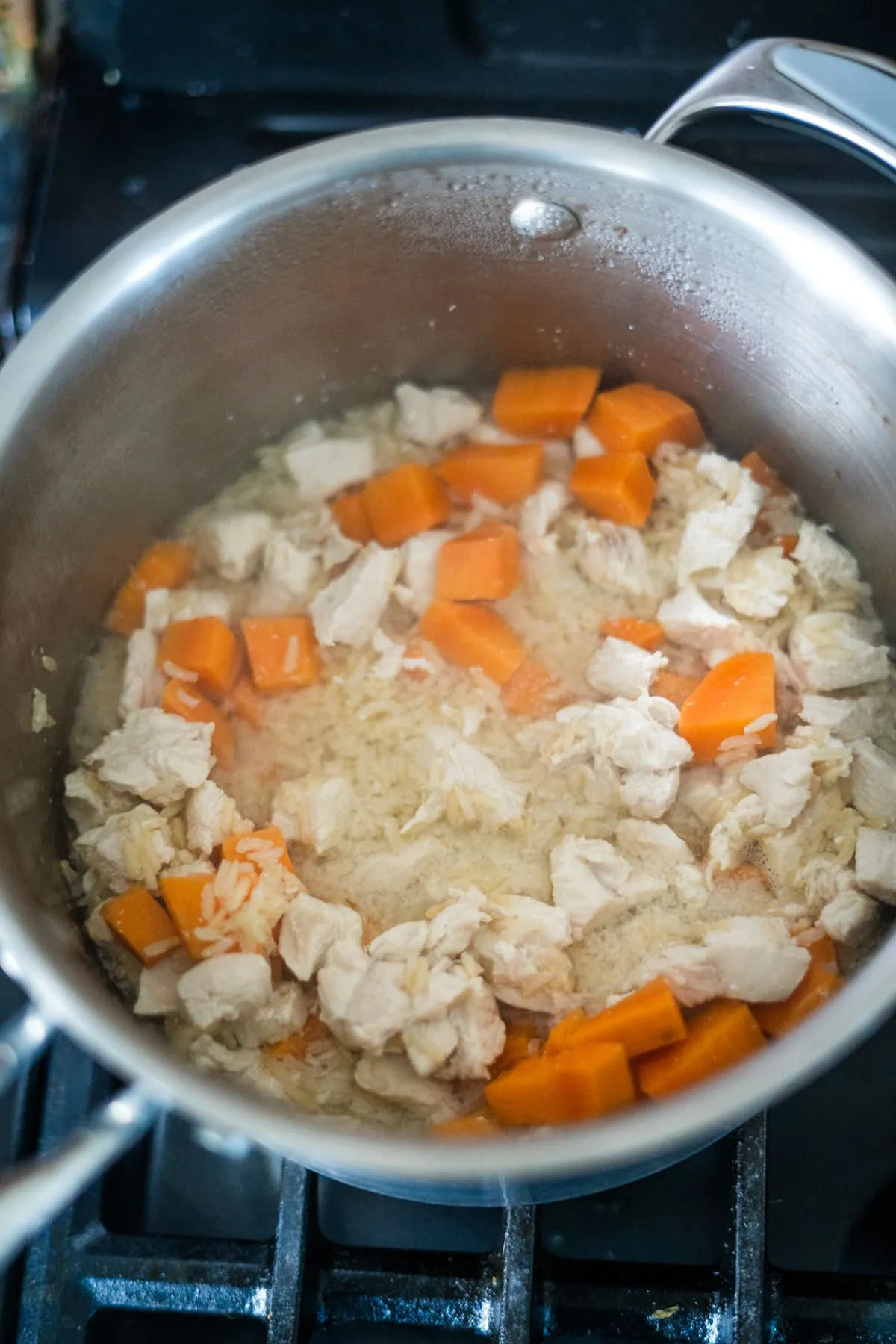 A pot of cooked rice with diced chicken, carrot pieces, and tender pumpkin sits on the stovetop.