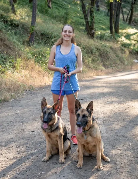 A white German Shepherd dog and another German Shepherd dog running together outdoors
