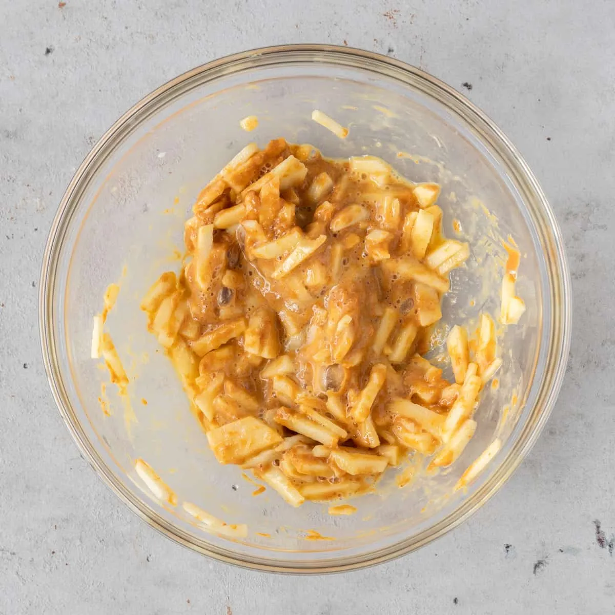 All dog cake ingredients, including chopped apple, peanut butter, egg, and baking powder, thoroughly mixed in a glass bowl