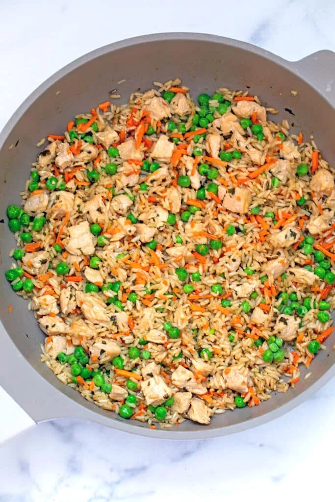 Chicken and rice mixed with carrots and peas in a skillet, ready to serve.
