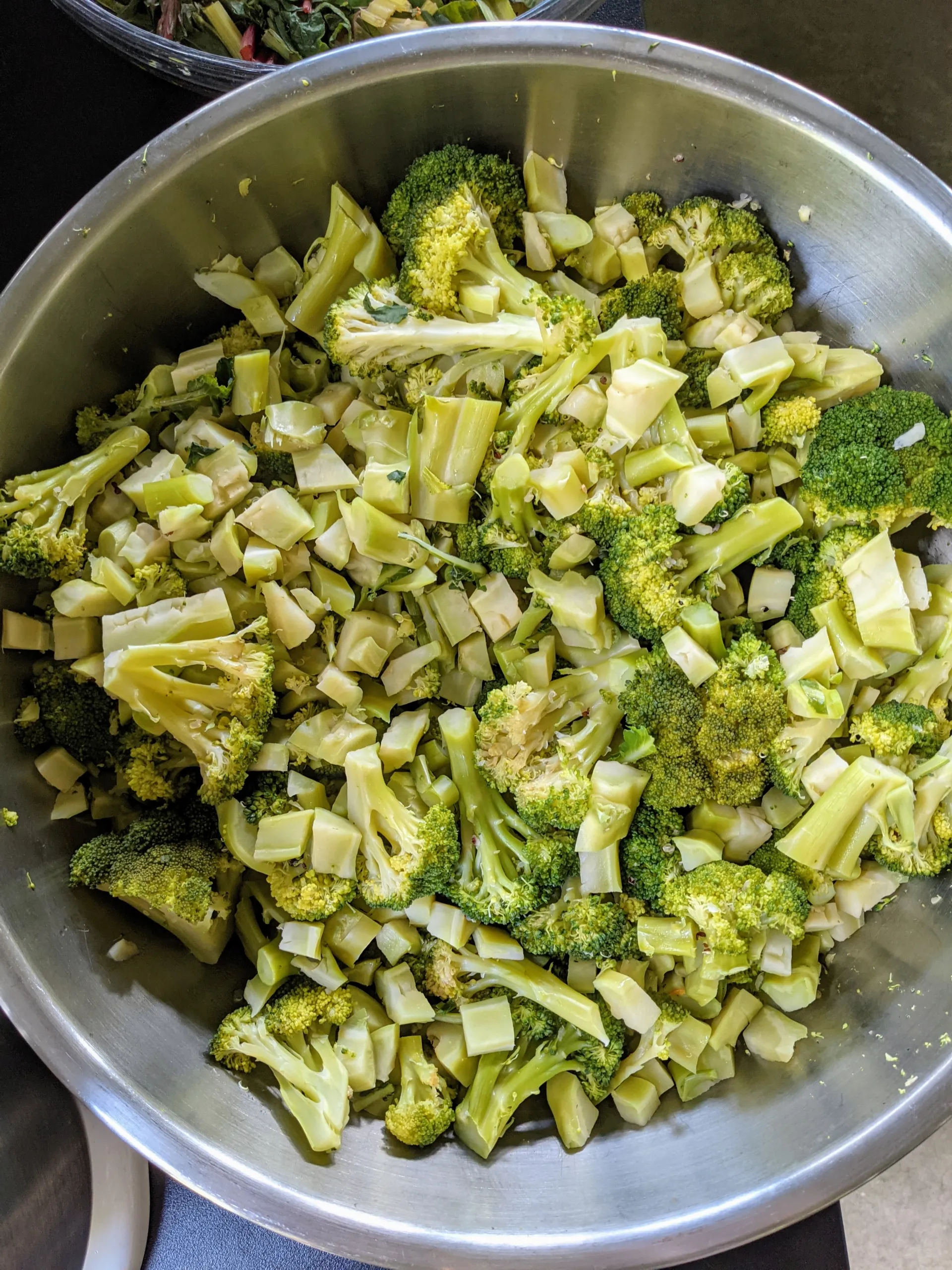 Cooked broccoli heads in a large stainless steel bowl
