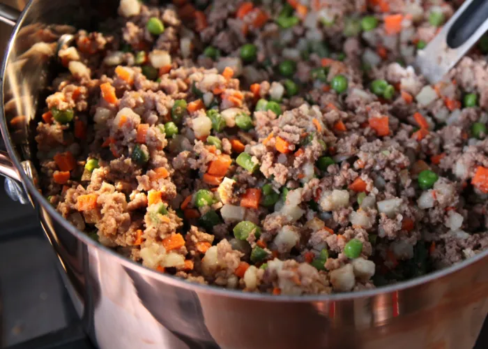 Cooked venison, sweet peas, and quinoa mixed in a bowl, drizzled with coconut oil