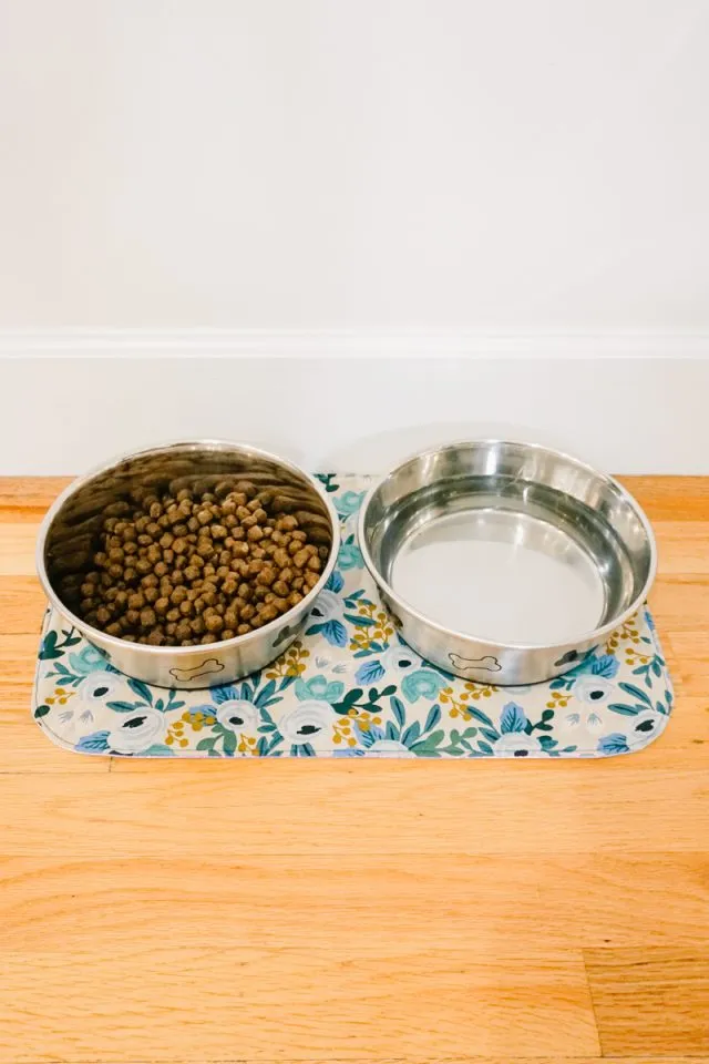 Finished DIY Dog Bowl Mat with two ceramic bowls on a wood floor