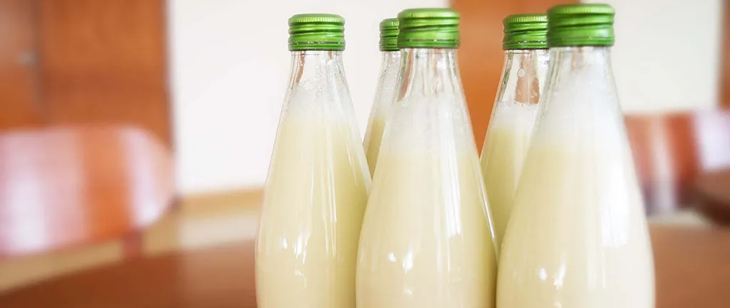 Five glass bottles of kefir with green caps sitting on a wooden table, ready for consumption