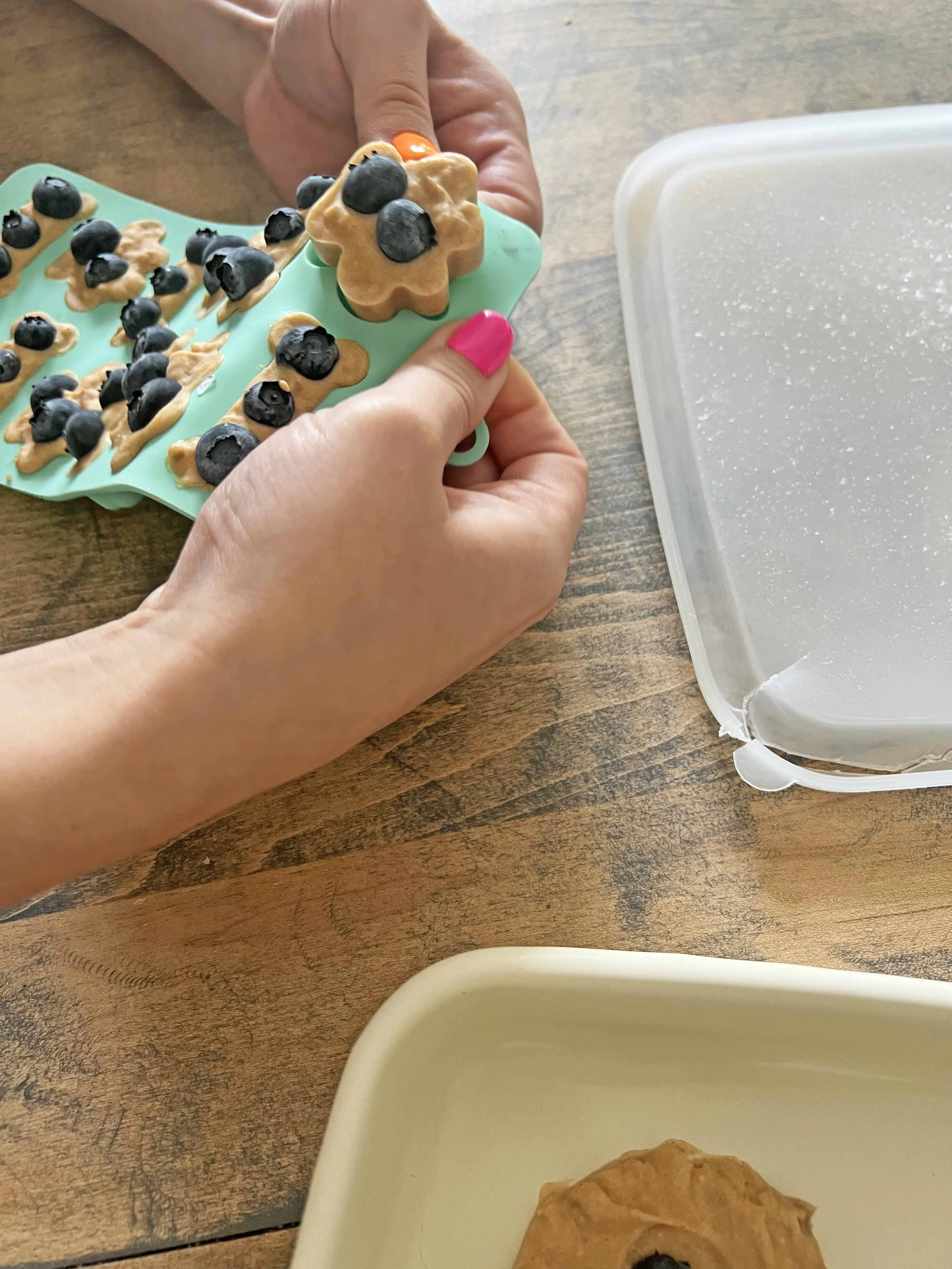 Frozen dog treats, shaped like paws and bones, being carefully popped out of a flexible silicone mold