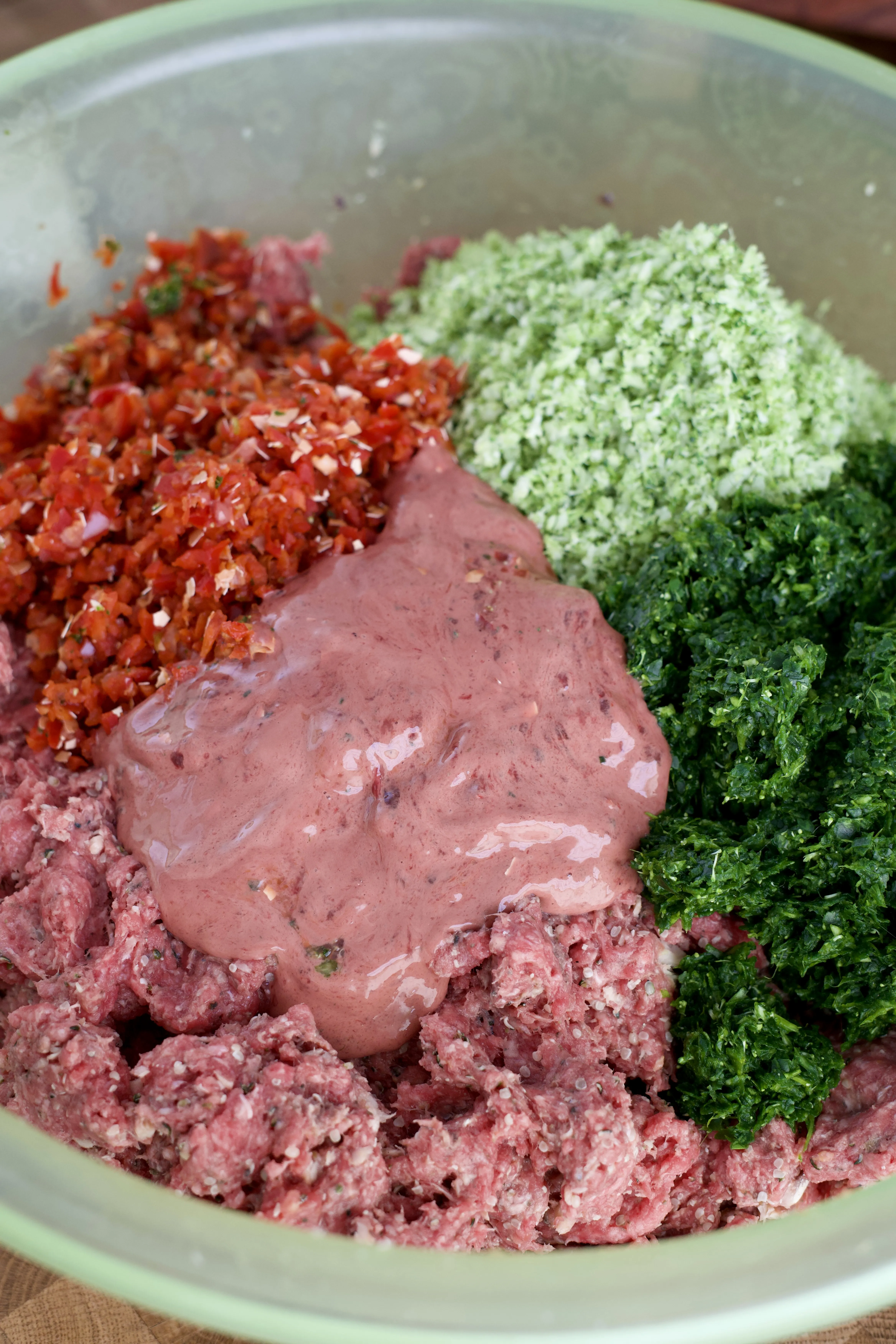 Mixing blended vegetables and liver with ground beef in a large bowl to create homemade dog food.