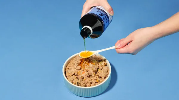 Pooch & Mutt Salmon Oil being poured onto a spoon over a bowl of dog food, against a pale blue background