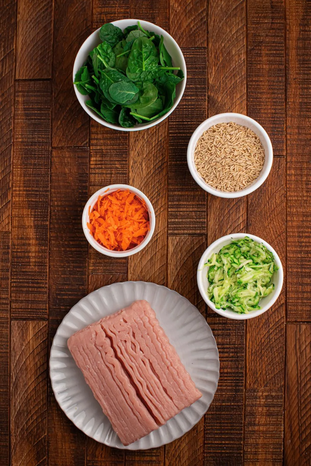 Separate containers holding fresh ingredients like lean ground turkey, brown rice, zucchini, carrots, and spinach for a healthy dog meal.