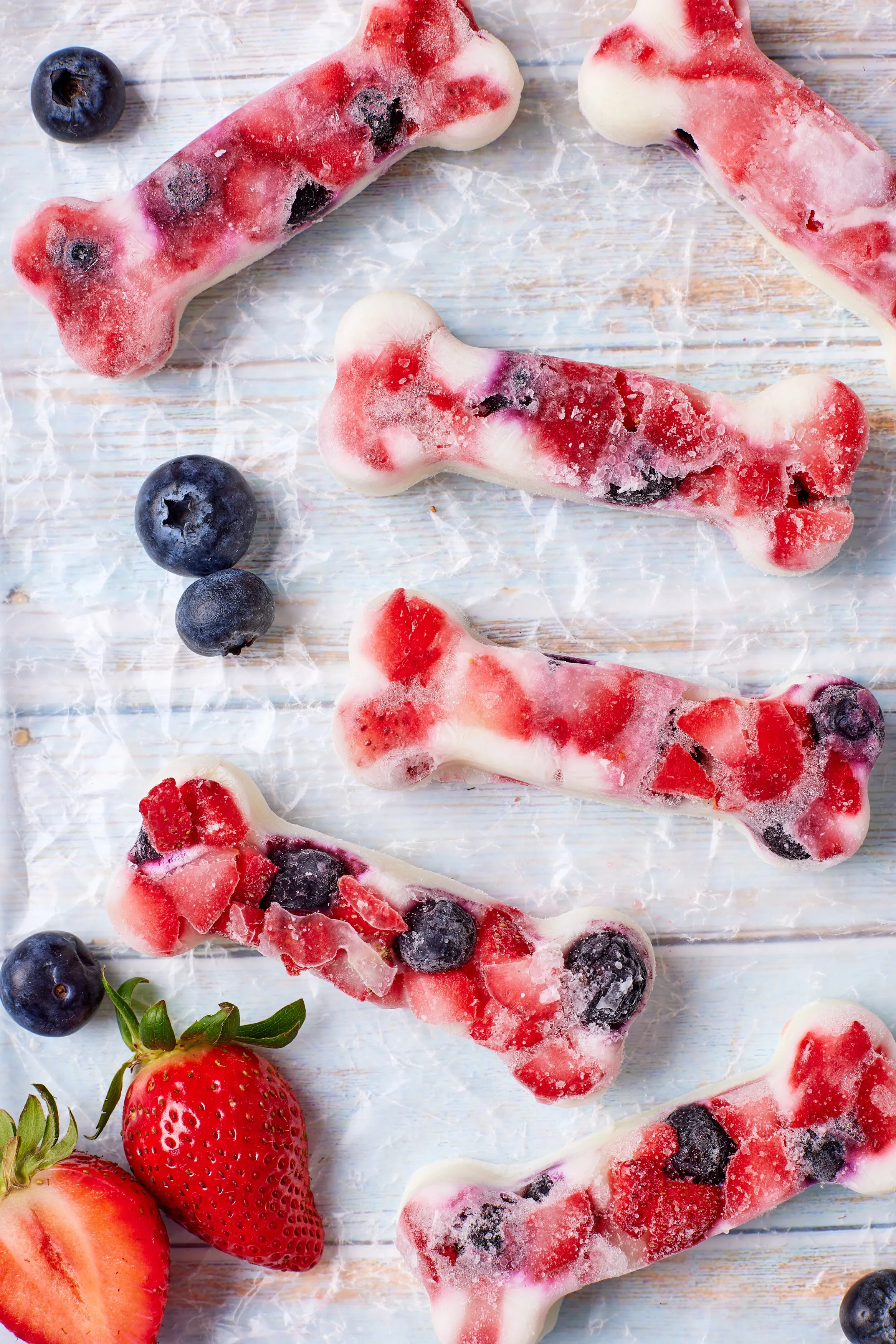 Six bone-shaped homemade frozen yogurt dog treats with strawberries and blueberries