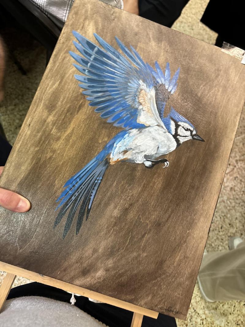 An attentive white and brown dog with blue eyes, clearly deaf, sitting on a green lawn and looking up intently at its owner's hand, which is poised to give a signal. The scene is bright and positive, focusing on the strong bond between them.