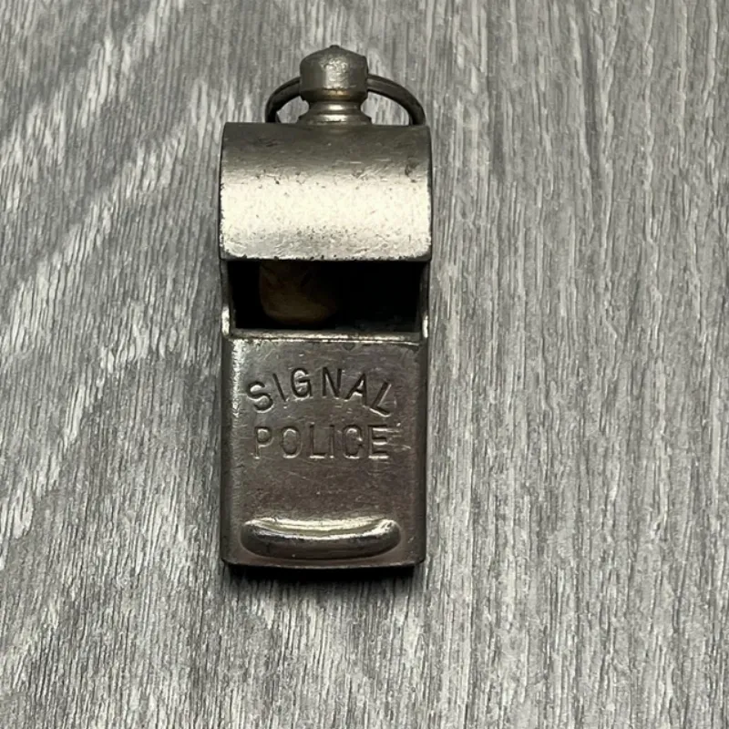 A close-up shot of three different types of dog training whistles—an ultrasonic, a pea whistle, and a pealess whistle—arranged neatly on a wooden surface.