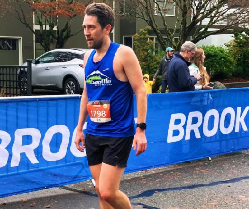A vibrant crowd cheering at Emerald Downs horse racing, with thoroughbreds rounding the final turn and Mount Rainier visible in the background.