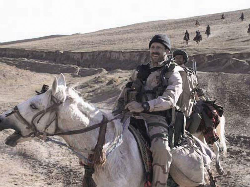 A depiction of a U.S. Green Beret from the horse soldiers real story using modern communications gear next to his horse to call in an air strike.