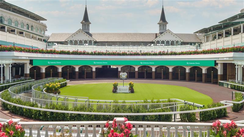 A wide-angle shot of Thoroughbred horses racing down the final stretch at Churchill Downs, with the iconic twin spires in the background, capturing the excitement of states with horse racing.